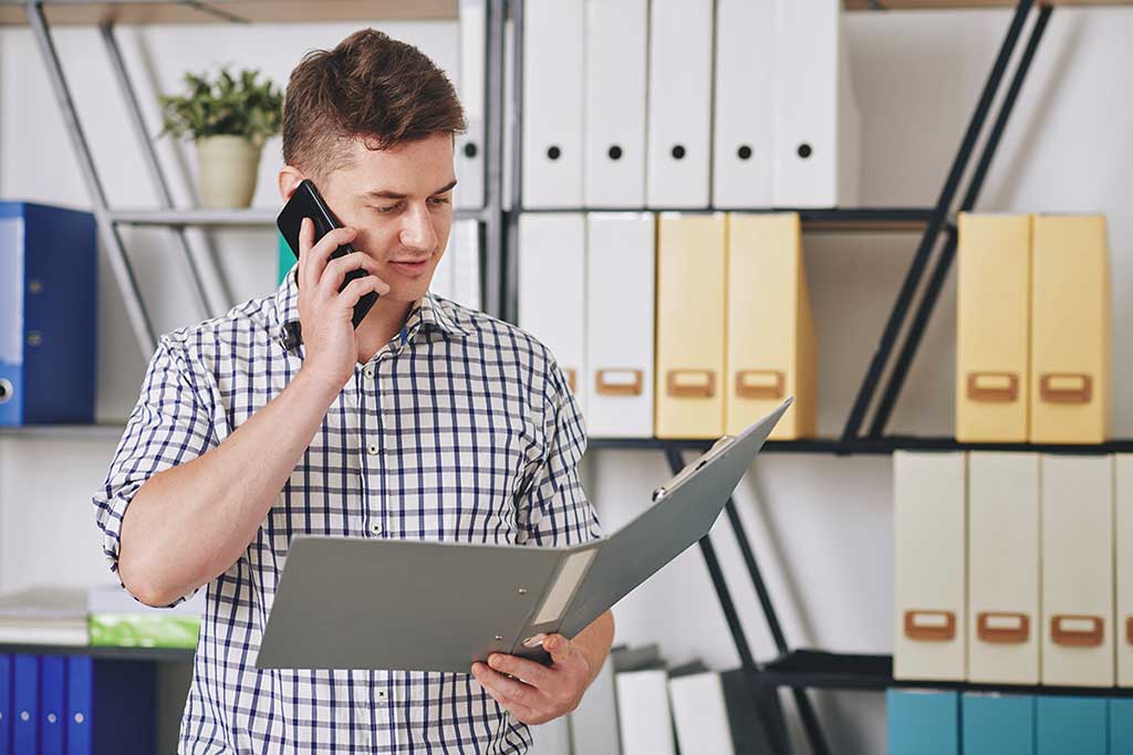 Ung mann står med en mappe som han ser i, mens han er på telefonen