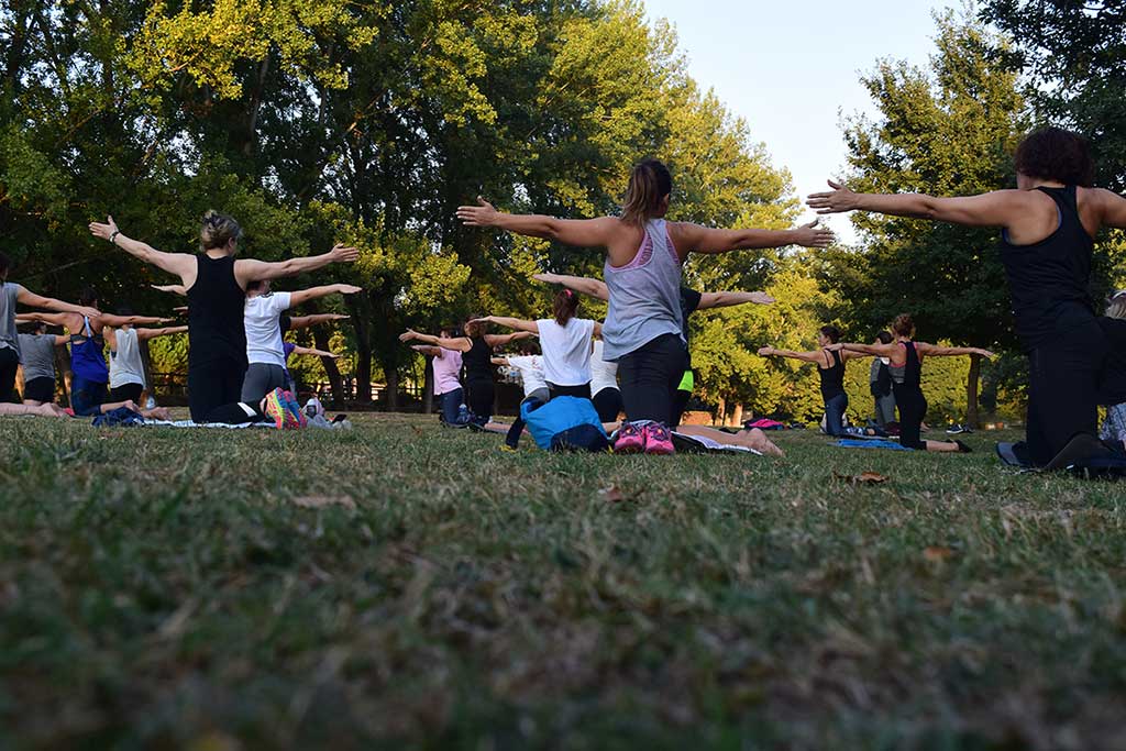 Mennesker som er samlet og dyrker yoga ute i en park.
